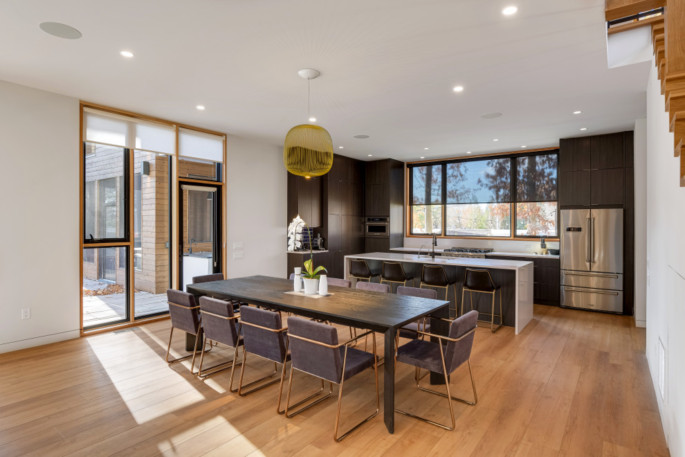 Cette image montre une salle à manger ouverte sur la cuisine design avec un mur blanc, un sol en bois brun, aucune cheminée et un sol marron.