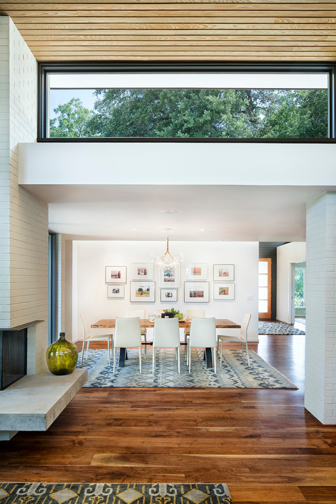 Cette photo montre une salle à manger tendance avec un mur blanc, un sol en bois brun, un manteau de cheminée en brique et une cheminée standard.