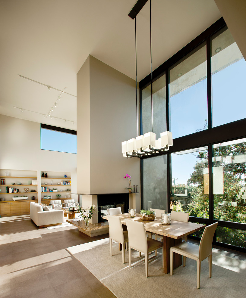 Cette photo montre une salle à manger ouverte sur le salon tendance avec un mur beige et une cheminée double-face.