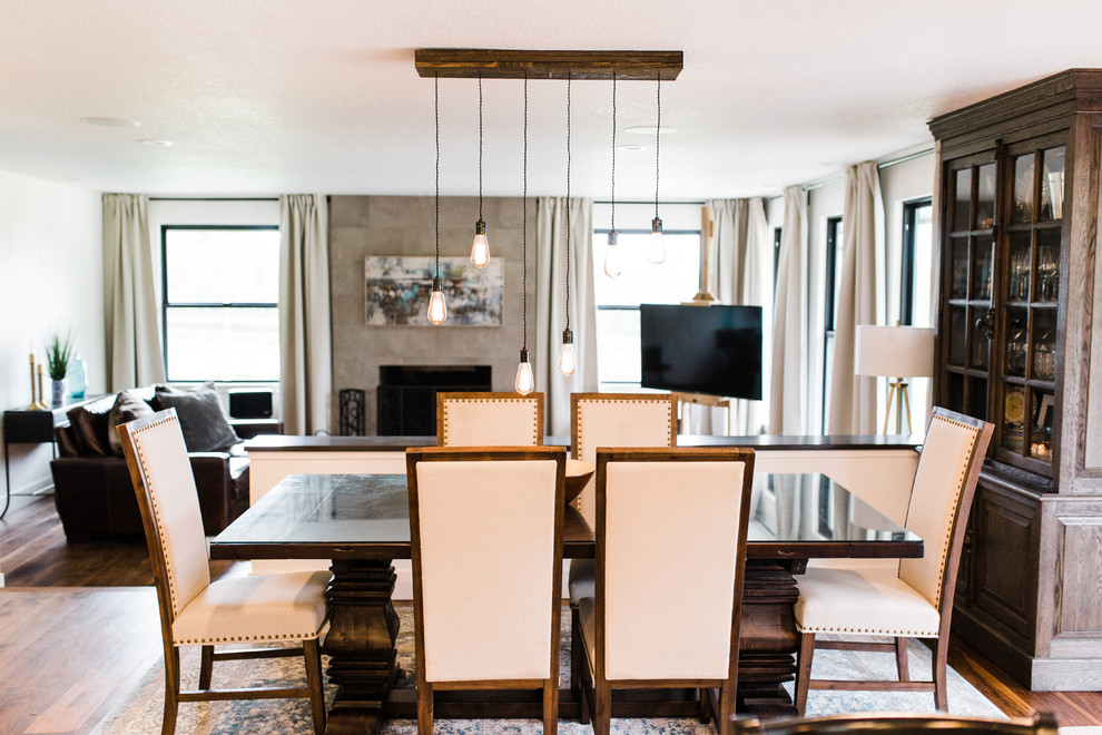Cette photo montre une salle à manger ouverte sur le salon chic de taille moyenne avec un mur blanc, un sol en bois brun, un manteau de cheminée en carrelage, un sol marron et une cheminée standard.