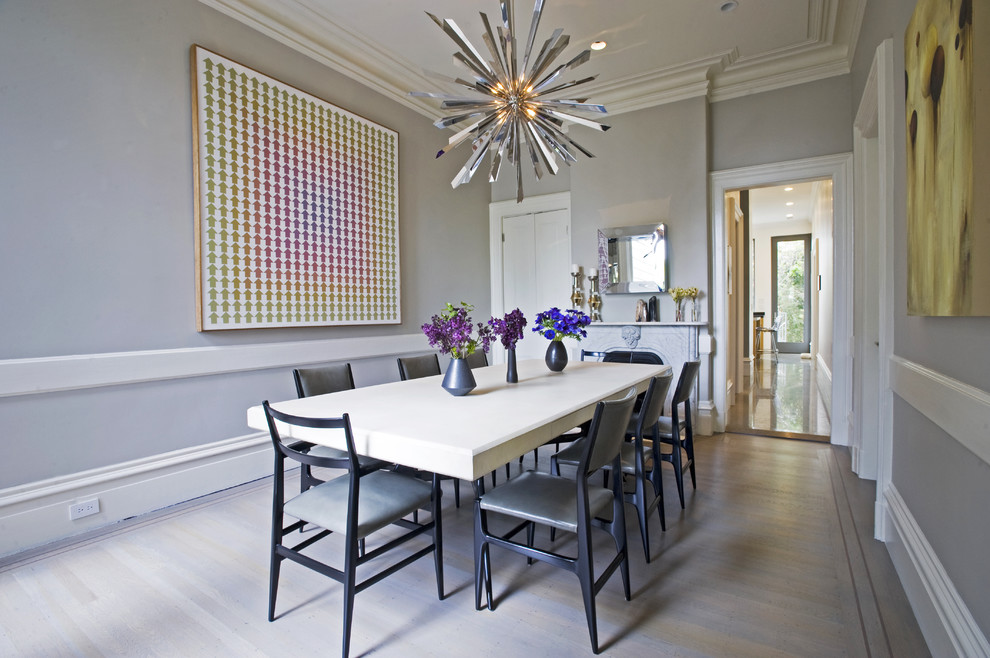 Idée de décoration pour une salle à manger minimaliste fermée avec un mur gris, un sol en bois brun et une cheminée standard.