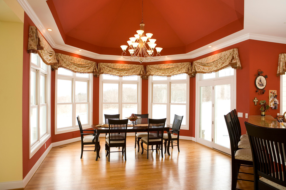 Foto di una grande sala da pranzo aperta verso la cucina tradizionale con pareti rosse, pavimento in legno massello medio e nessun camino