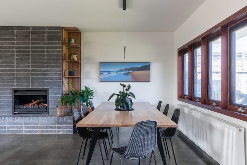 Aménagement d'une salle à manger contemporaine avec un mur blanc, sol en béton ciré, une cheminée standard, un manteau de cheminée en brique et un sol gris.