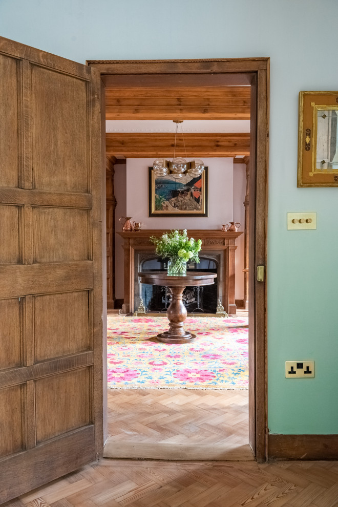 Diseño de comedor bohemio grande cerrado con paredes verdes, suelo de madera clara, todas las chimeneas, marco de chimenea de piedra, suelo beige y papel pintado