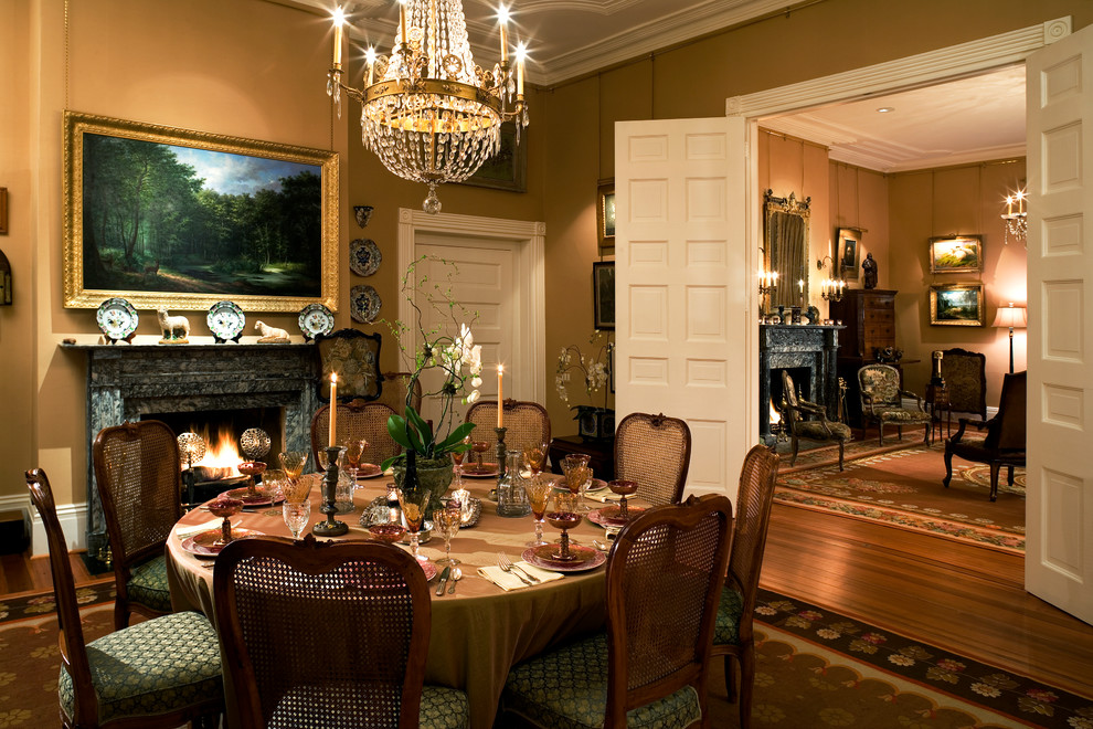 Exemple d'une salle à manger chic fermée avec un mur beige, un sol en bois brun, une cheminée standard et éclairage.