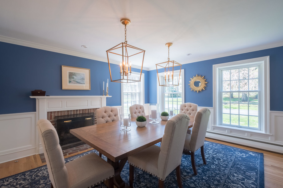 Exemple d'une salle à manger chic fermée et de taille moyenne avec un mur bleu, un sol en bois brun, une cheminée standard, un manteau de cheminée en bois et un sol marron.
