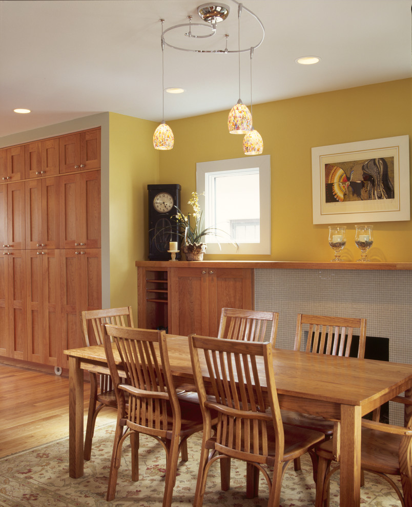 Cette photo montre une salle à manger ouverte sur le salon chic de taille moyenne avec un mur jaune, un sol en bois brun, une cheminée standard et un manteau de cheminée en carrelage.