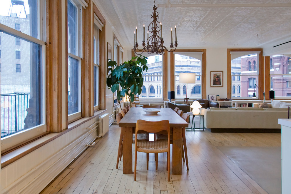 Immagine di una sala da pranzo aperta verso il soggiorno industriale con pareti bianche e parquet chiaro
