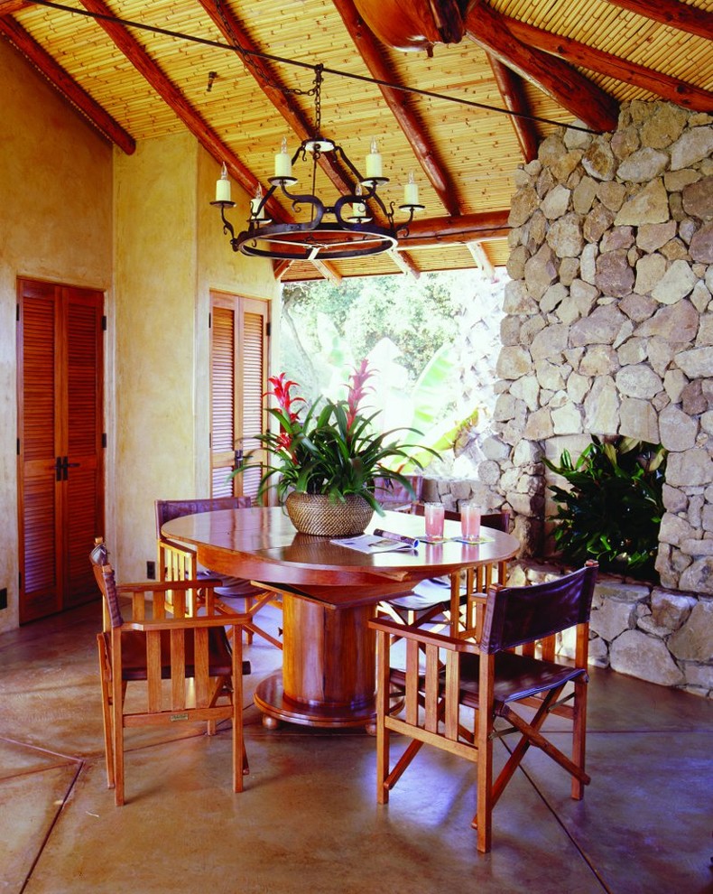 Immagine di una sala da pranzo tropicale con pavimento in cemento e cornice del camino in pietra