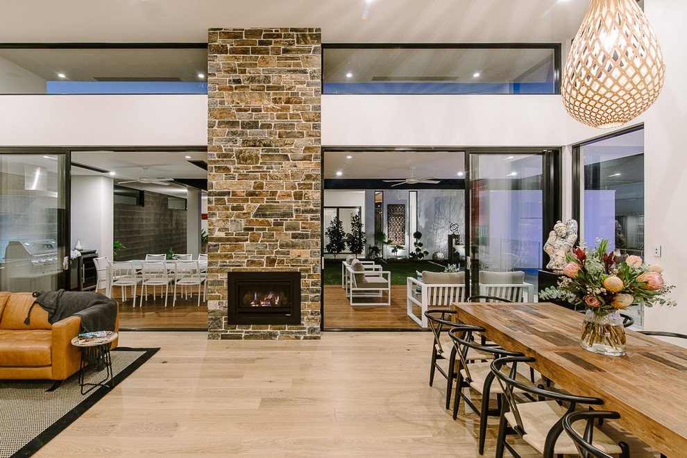 Cette photo montre une grande salle à manger ouverte sur le salon tendance avec un mur blanc, parquet clair, une cheminée double-face et un manteau de cheminée en pierre.