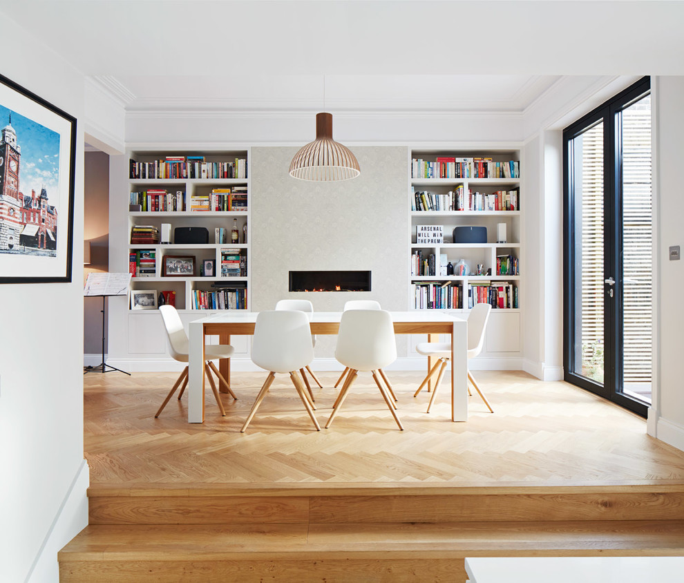 Mid-sized trendy light wood floor and beige floor kitchen/dining room combo photo in London with white walls, a ribbon fireplace and a plaster fireplace