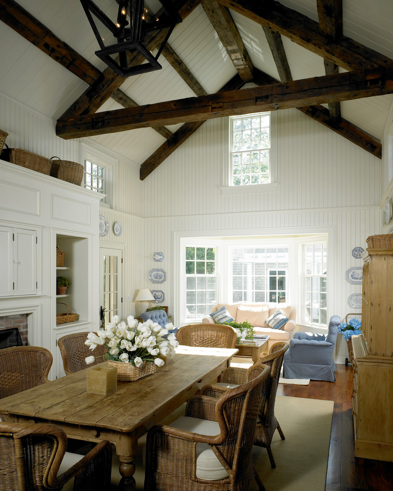 Exemple d'une salle à manger ouverte sur le salon chic de taille moyenne avec un mur blanc, un sol en bois brun, une cheminée standard et un manteau de cheminée en brique.