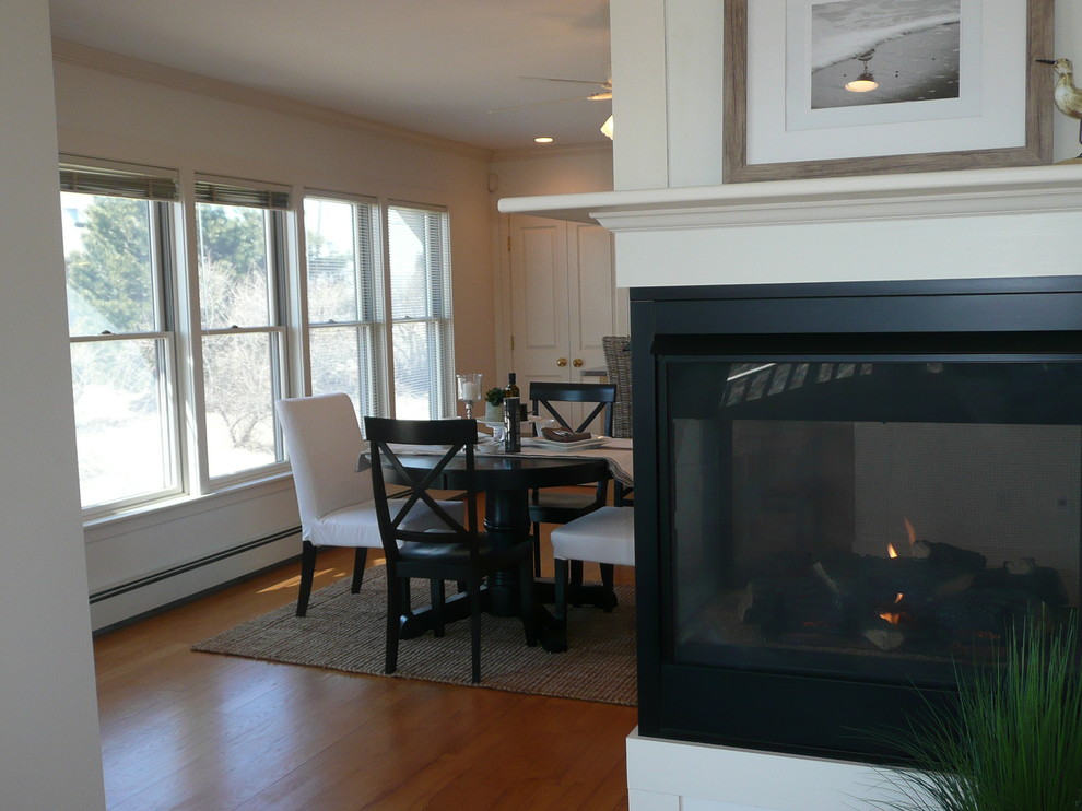 This is an example of a medium sized beach style kitchen/dining room in Boston with white walls, medium hardwood flooring and a two-sided fireplace.