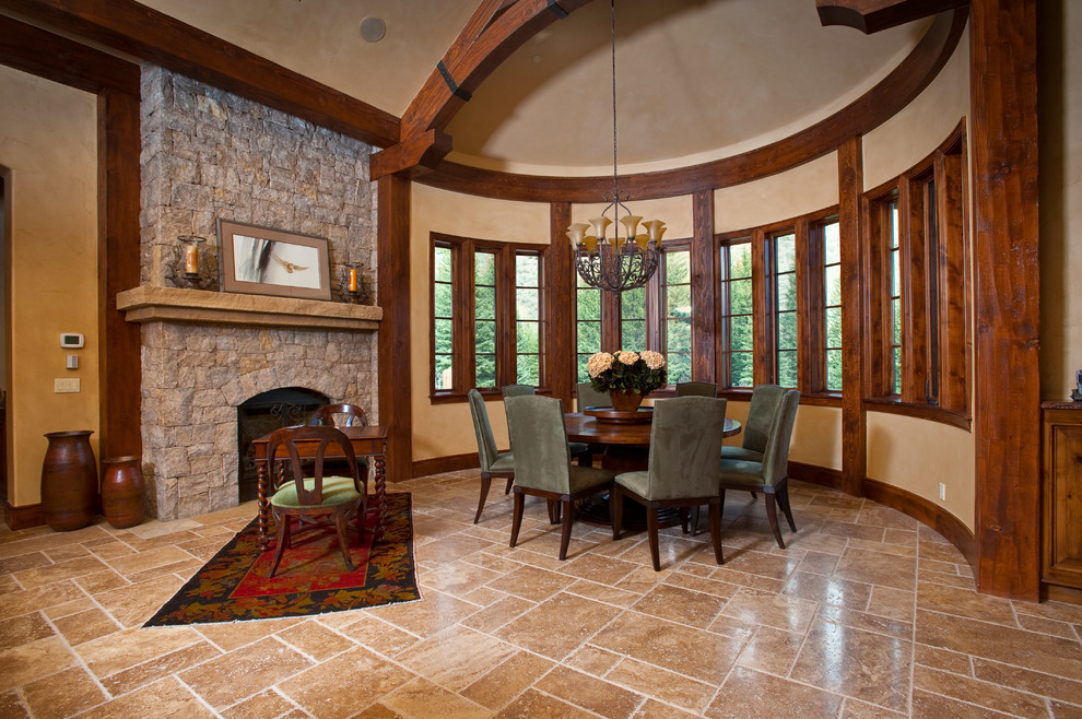 Exemple d'une très grande salle à manger ouverte sur la cuisine montagne avec un mur beige, un manteau de cheminée en pierre, une cheminée standard, un sol en travertin, un sol beige et un plafond voûté.