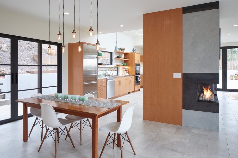 Réalisation d'une salle à manger ouverte sur la cuisine design de taille moyenne avec un mur blanc, un sol en carrelage de porcelaine, une cheminée d'angle, un manteau de cheminée en plâtre et un sol gris.