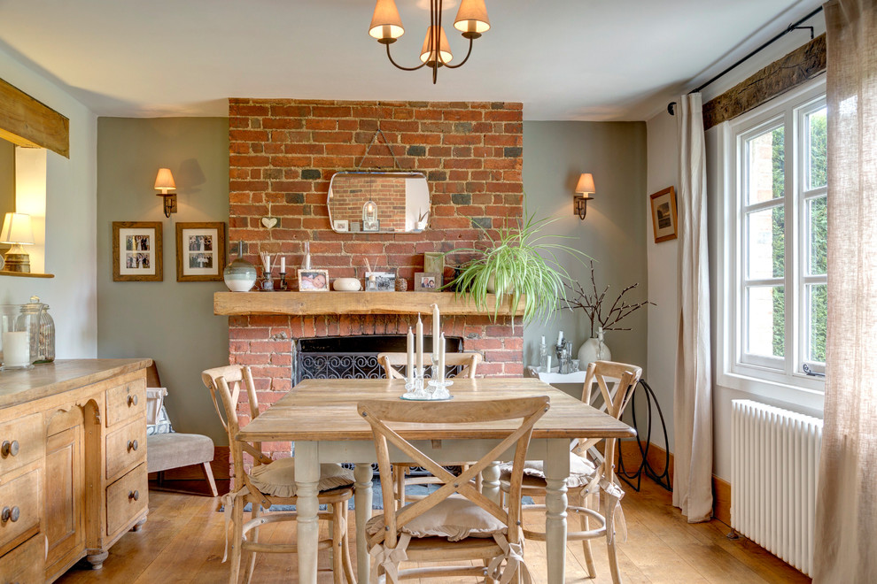 Design ideas for a medium sized rural enclosed dining room in Kent with green walls, light hardwood flooring, a standard fireplace, a brick fireplace surround and brown floors.