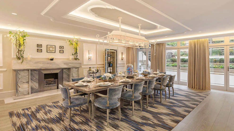 This is an example of an expansive contemporary enclosed dining room in London with beige walls, light hardwood flooring, a standard fireplace, a stone fireplace surround and brown floors.
