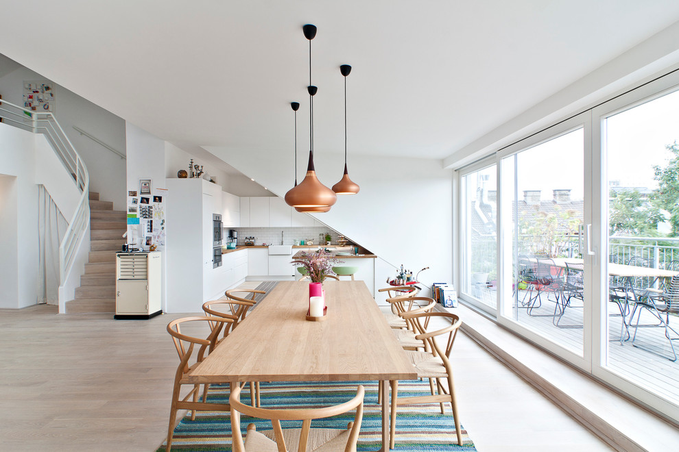 Aménagement d'une salle à manger ouverte sur la cuisine scandinave avec un mur blanc et parquet clair.