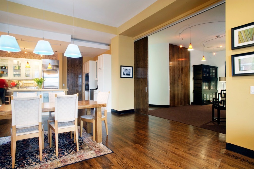Cette photo montre une salle à manger ouverte sur la cuisine tendance de taille moyenne avec un mur jaune, un sol en bois brun et un sol marron.