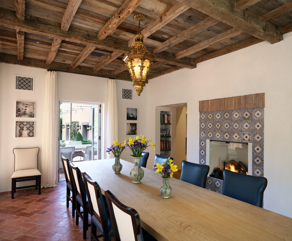 Foto de comedor mediterráneo cerrado con paredes blancas, suelo de baldosas de terracota, marco de chimenea de baldosas y/o azulejos, suelo naranja y cortinas