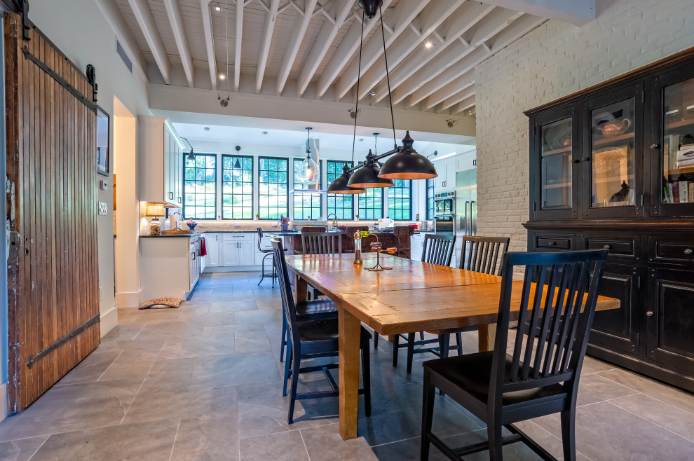 Foto di una grande sala da pranzo aperta verso la cucina country con pavimento in gres porcellanato, pareti bianche e pavimento grigio