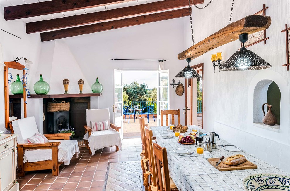 Foto di una sala da pranzo aperta verso il soggiorno mediterranea con pareti bianche, pavimento in terracotta e stufa a legna