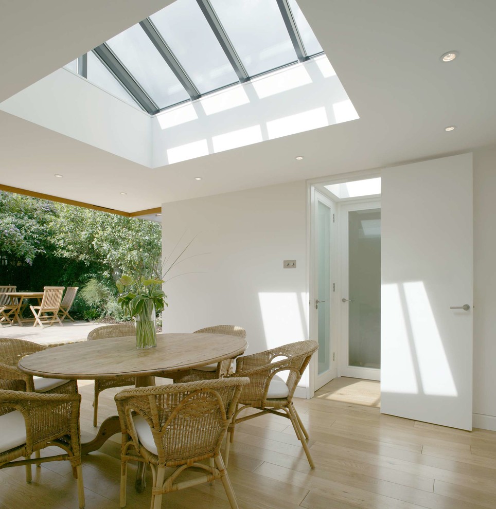 Design ideas for a small contemporary open plan dining room in London with white walls and light hardwood flooring.