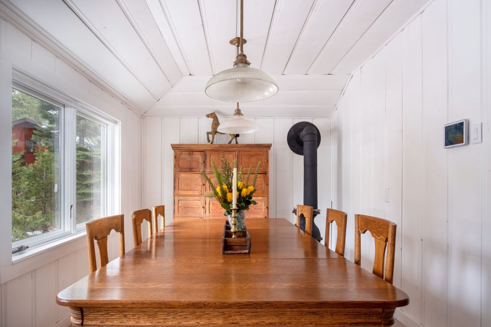 Foto de comedor de cocina tradicional de tamaño medio con paredes blancas, suelo de madera clara, estufa de leña, marco de chimenea de madera y suelo beige