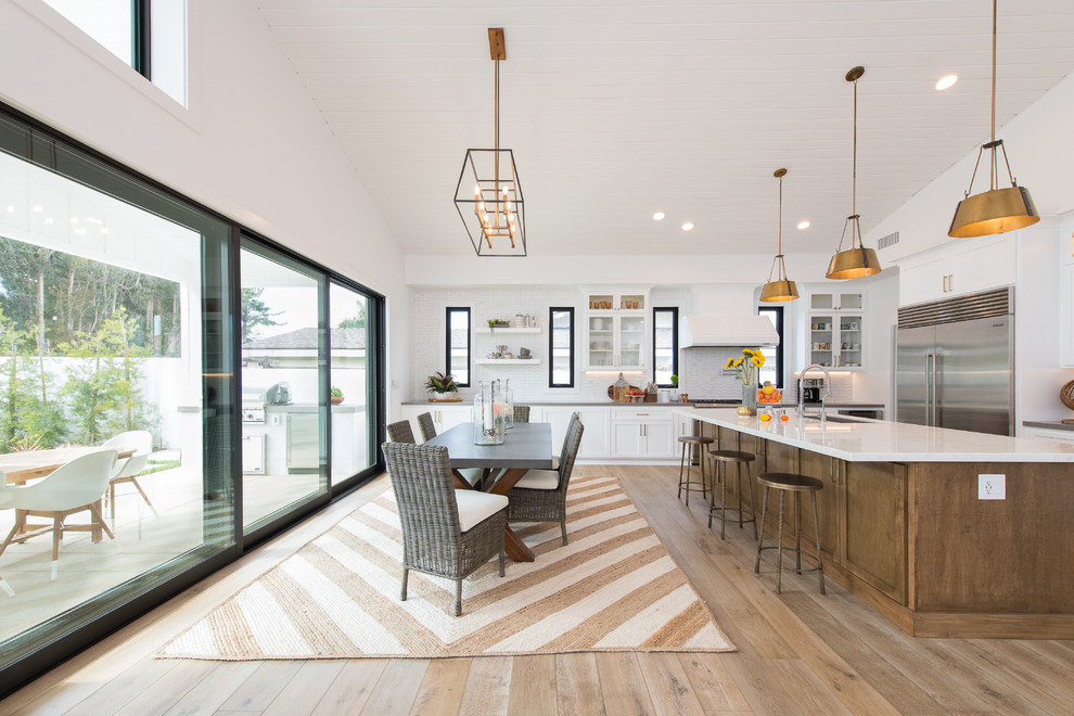 Cette image montre une grande salle à manger ouverte sur la cuisine rustique avec un mur blanc, un sol en bois brun, aucune cheminée, un manteau de cheminée en bois et un sol marron.