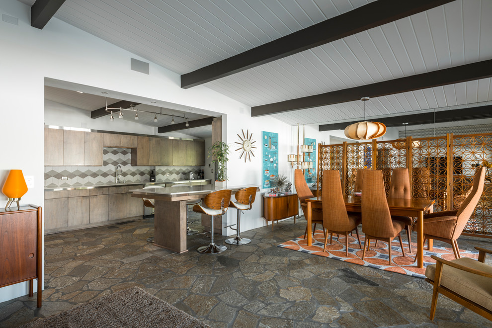 Cette image montre une salle à manger ouverte sur le salon vintage de taille moyenne avec un mur blanc, un sol en ardoise, une cheminée standard, un manteau de cheminée en plâtre et un sol marron.