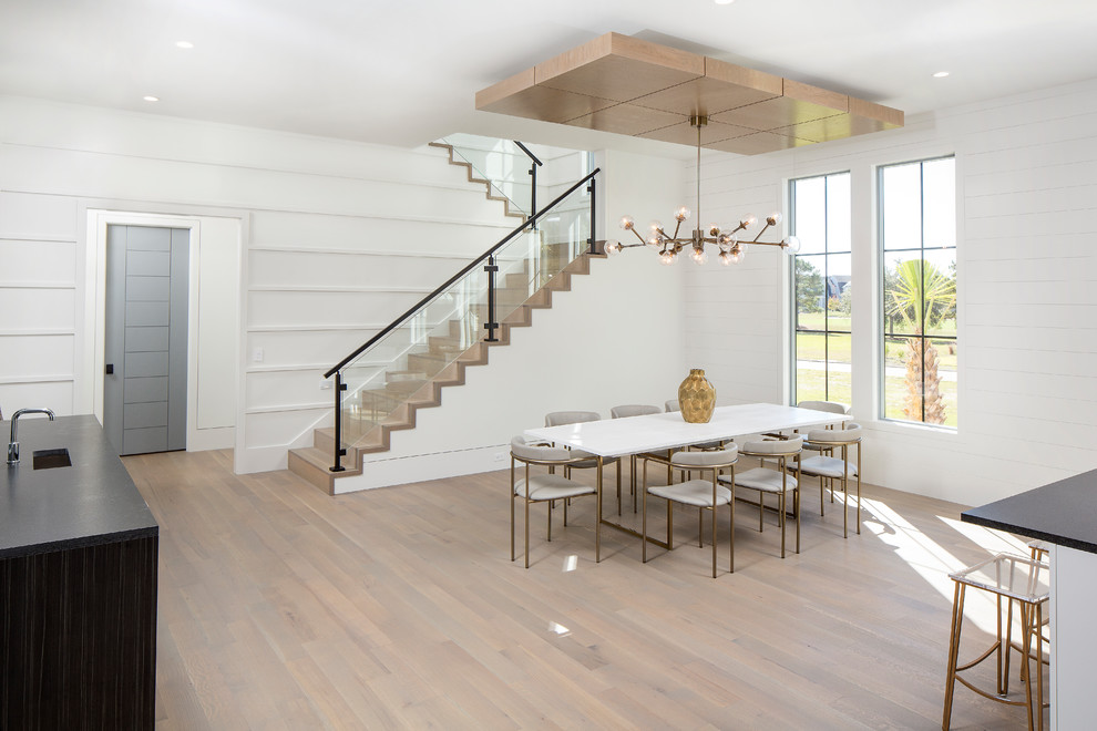 Cette image montre une grande salle à manger ouverte sur la cuisine design avec un mur blanc, un sol en bois brun, une cheminée standard, un manteau de cheminée en métal et un sol gris.