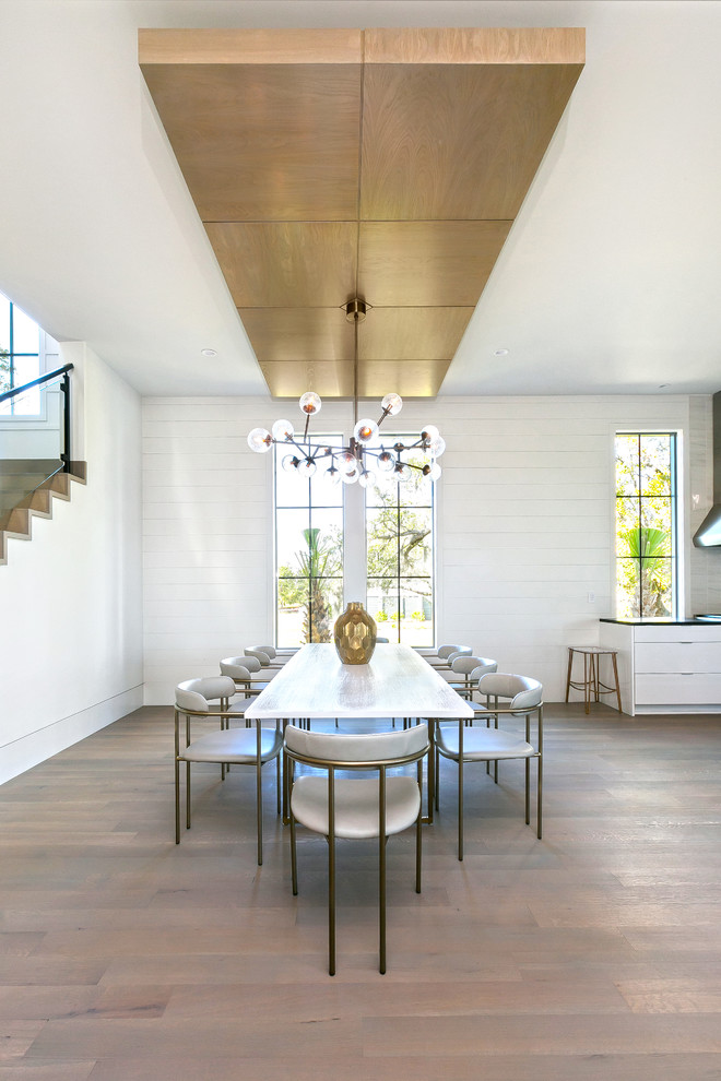 Inspiration pour une grande salle à manger ouverte sur la cuisine design avec un mur blanc, un sol en bois brun, une cheminée standard, un manteau de cheminée en métal et un sol gris.