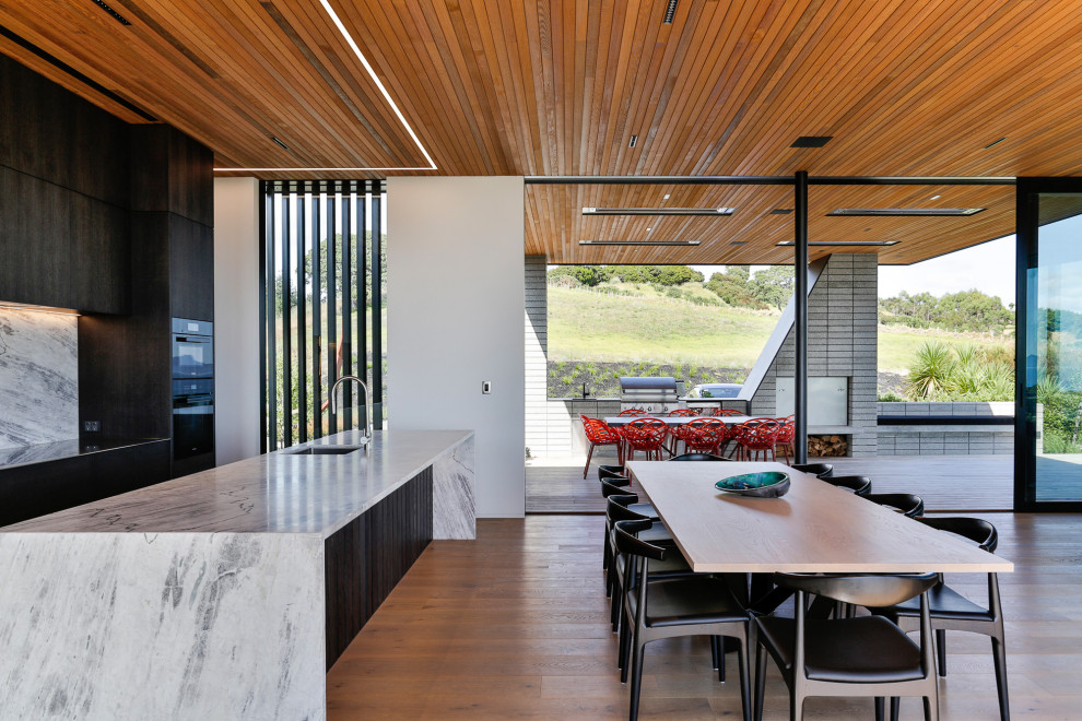 Cette image montre une grande salle à manger ouverte sur la cuisine design avec un mur blanc, un sol en bois brun, un sol marron et un plafond en bois.