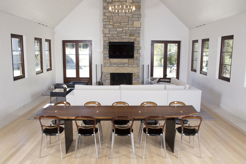 Photo of a medium sized contemporary open plan dining room in New York with white walls, light hardwood flooring, a standard fireplace and a stone fireplace surround.