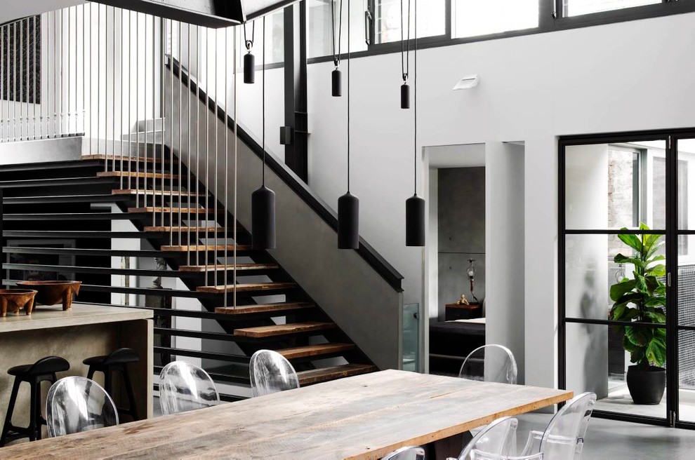 Cette image montre une grande salle à manger ouverte sur la cuisine urbaine avec un mur blanc, sol en béton ciré, aucune cheminée et un sol gris.