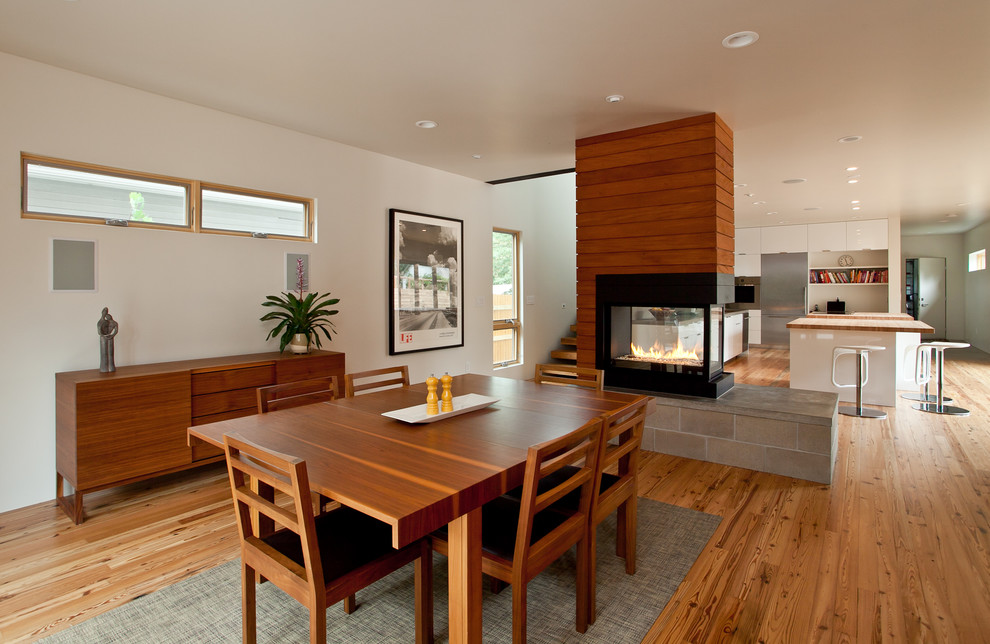 Пример оригинального дизайна: кухня-столовая в современном стиле с белыми стенами, паркетным полом среднего тона и двусторонним камином