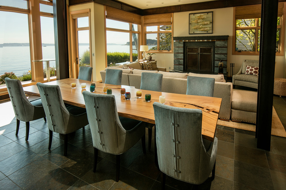 Cette image montre une grande salle à manger ouverte sur le salon marine avec un mur beige, un sol en ardoise, une cheminée standard, un manteau de cheminée en carrelage et un sol gris.