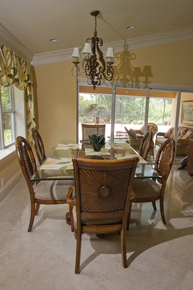 Immagine di una sala da pranzo tropicale con pareti gialle, pavimento in marmo, camino classico, cornice del camino in intonaco e pavimento beige