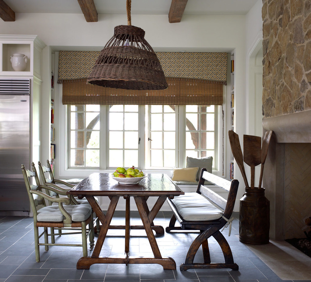 Exemple d'une salle à manger ouverte sur la cuisine chic avec un mur blanc, un manteau de cheminée en pierre et un sol en carrelage de céramique.