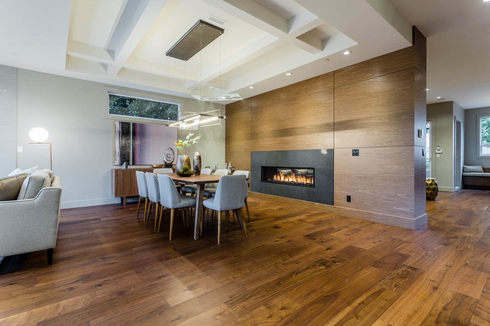 Idées déco pour une salle à manger ouverte sur le salon contemporaine avec un sol en bois brun, une cheminée double-face et un manteau de cheminée en bois.