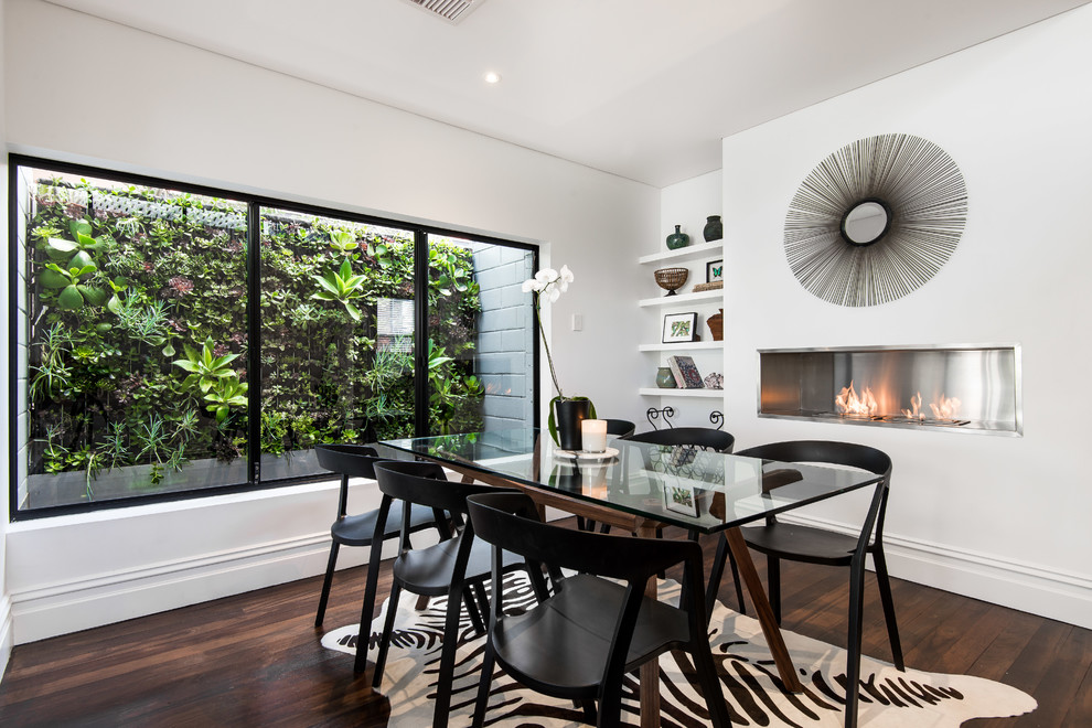 Cette image montre une petite salle à manger ouverte sur la cuisine design avec un mur blanc, parquet foncé et un manteau de cheminée en métal.