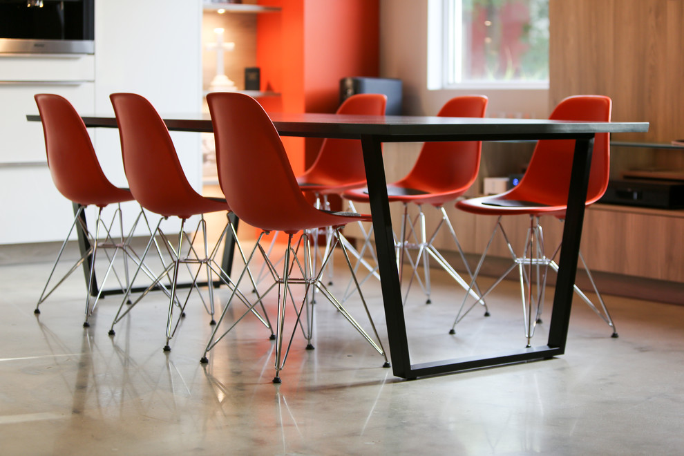 Cette image montre une grande salle à manger ouverte sur la cuisine minimaliste avec un mur orange, sol en béton ciré et un sol gris.
