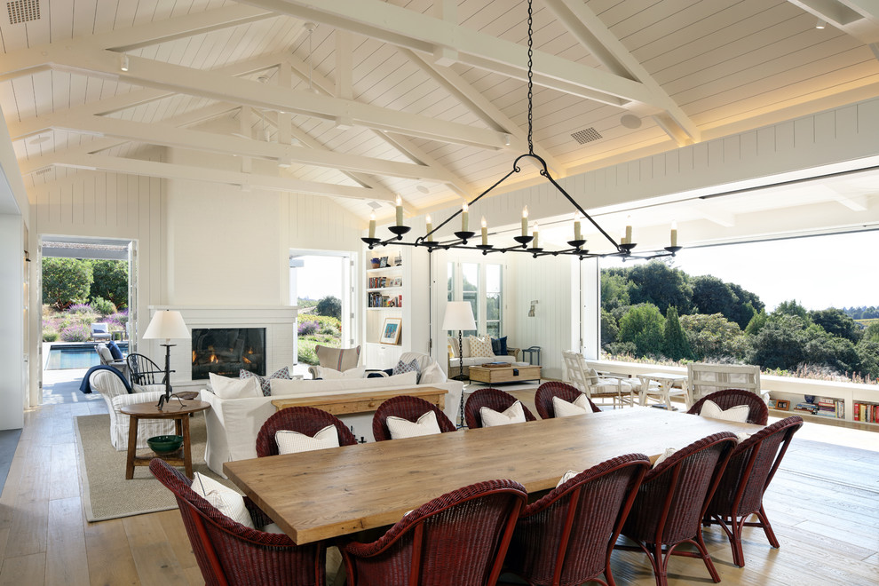 Idée de décoration pour une très grande salle à manger ouverte sur le salon champêtre avec un mur blanc, un sol en bois brun, une cheminée standard, un manteau de cheminée en brique et éclairage.