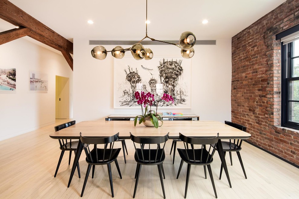 This is an example of an industrial dining room in New York with white walls and light hardwood flooring.