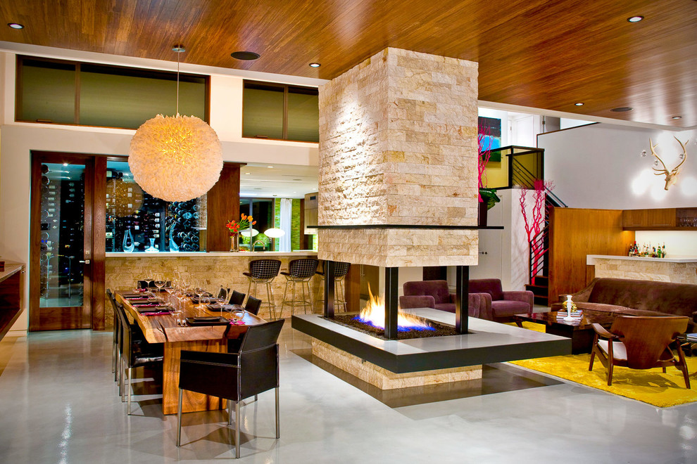 Imagen de comedor contemporáneo abierto con paredes blancas, suelo de cemento y chimenea de doble cara