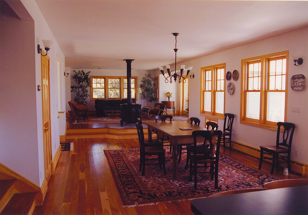 Пример оригинального дизайна: большая гостиная-столовая в викторианском стиле с белыми стенами, светлым паркетным полом, печью-буржуйкой и фасадом камина из металла