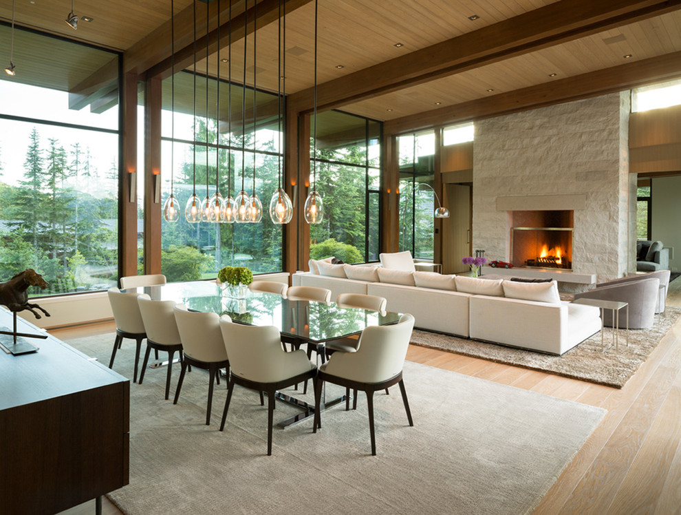 Cette image montre une très grande salle à manger ouverte sur le salon design avec parquet clair, une cheminée standard, un manteau de cheminée en pierre et un sol beige.