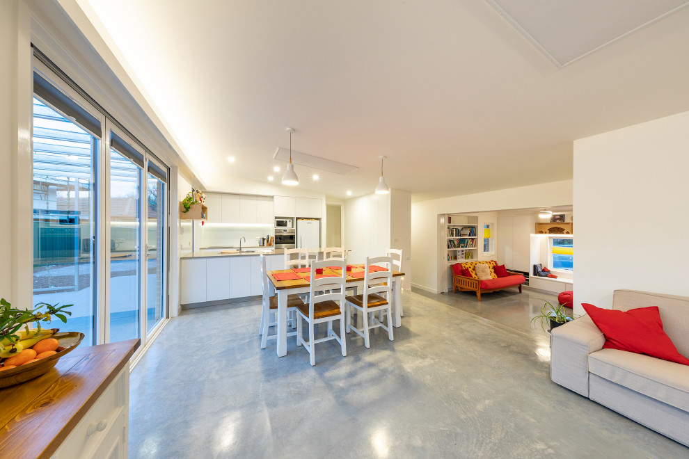 Foto di una piccola sala da pranzo aperta verso il soggiorno contemporanea con pareti bianche, pavimento in cemento e pavimento grigio