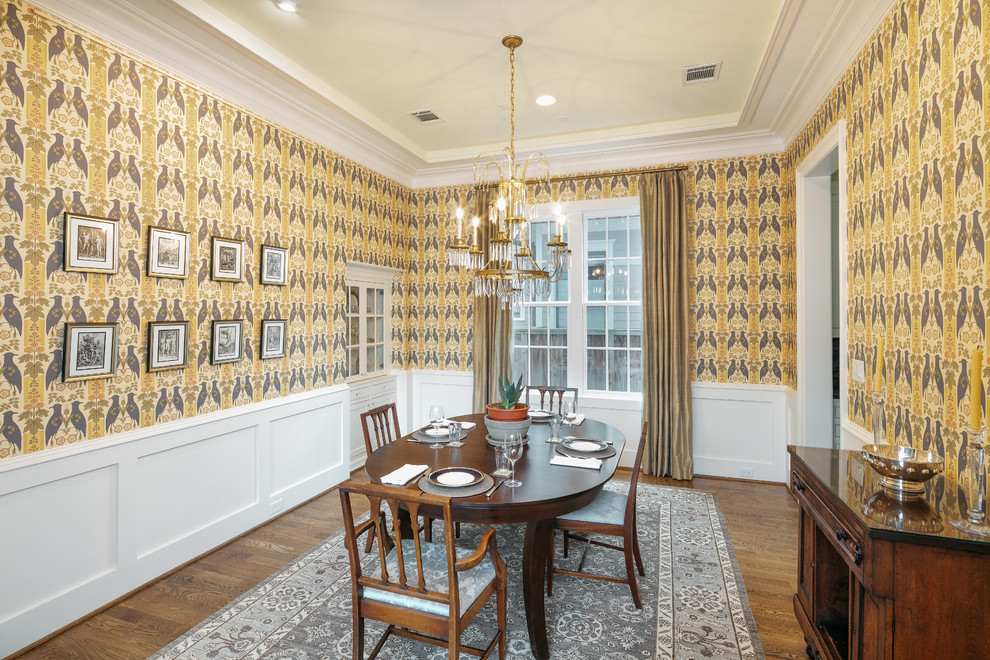 Geschlossenes Klassisches Esszimmer mit gelber Wandfarbe, dunklem Holzboden, braunem Boden und Tapetenwänden in Houston