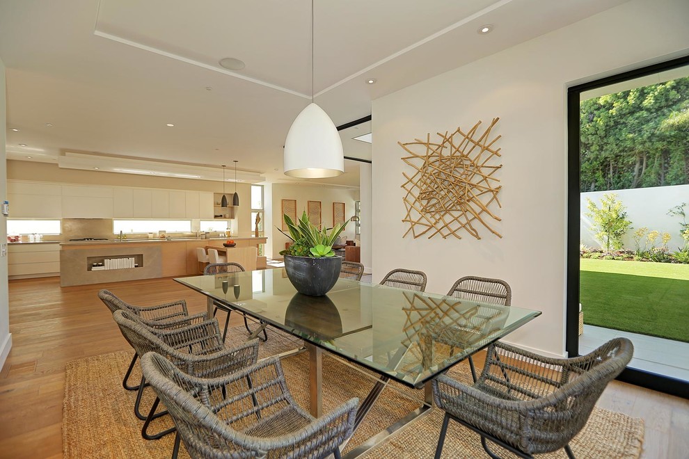 Aménagement d'une grande salle à manger ouverte sur la cuisine moderne avec un mur blanc et un sol en bois brun.
